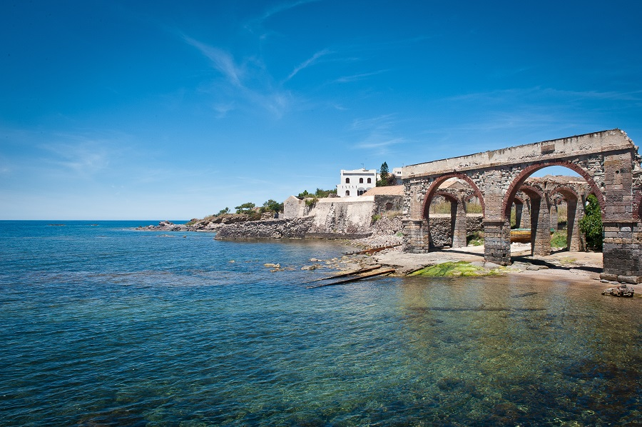 La costa di Portoscuso: scogli, mare trasparente e vecchie arcate in pietra.